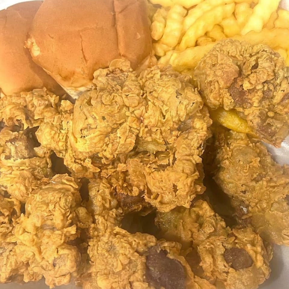 Foam container filled with crispy fried chicken, curly fries, and two bread rolls.