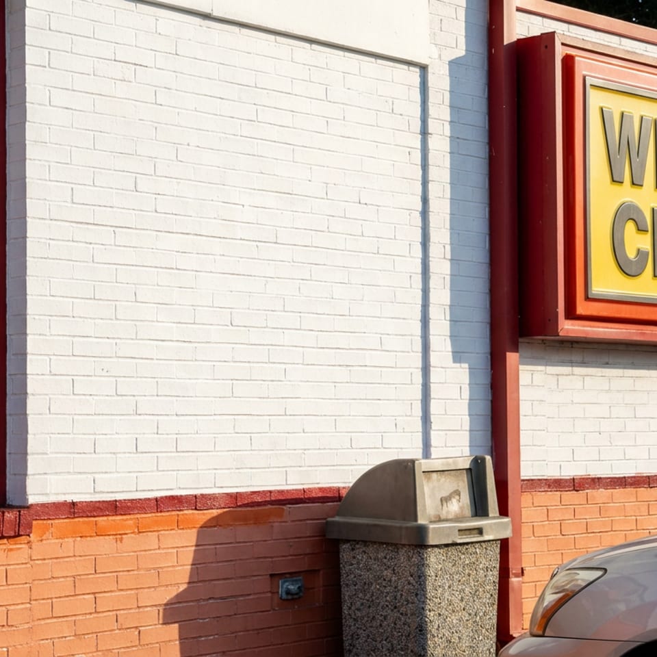 Williams Chicken restaurant exterior with a fried chicken value-pack advertisement, wall-mounted sign, trash bin, and parked car.
