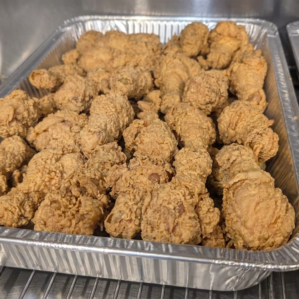 Aluminum trays filled with golden-brown, crispy fried chicken pieces in a restaurant warming station.