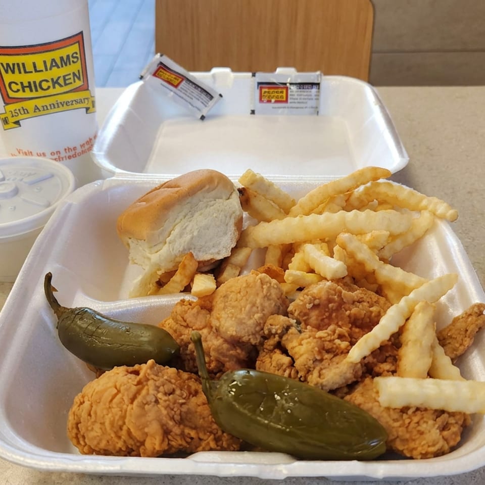 Williams Chicken takeout meal with fried chicken, crinkle-cut fries, jalapeños, a roll, drink, and open foam containers on a restaurant table.