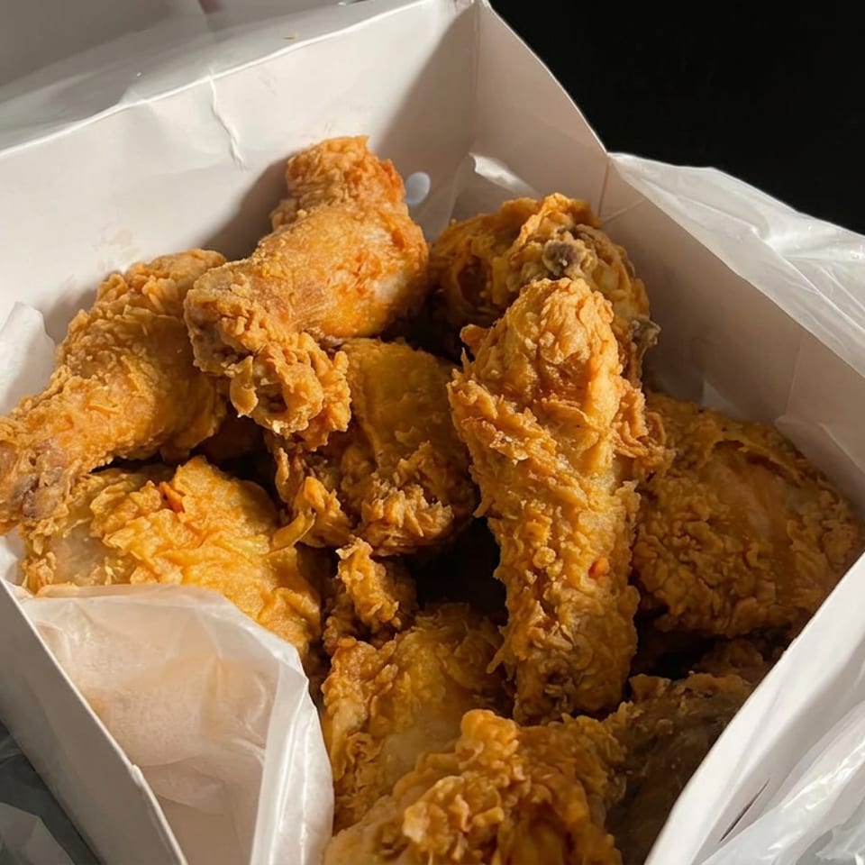 Open takeout box filled with crispy golden fried chicken pieces, including drumsticks, wings, and breast portions.