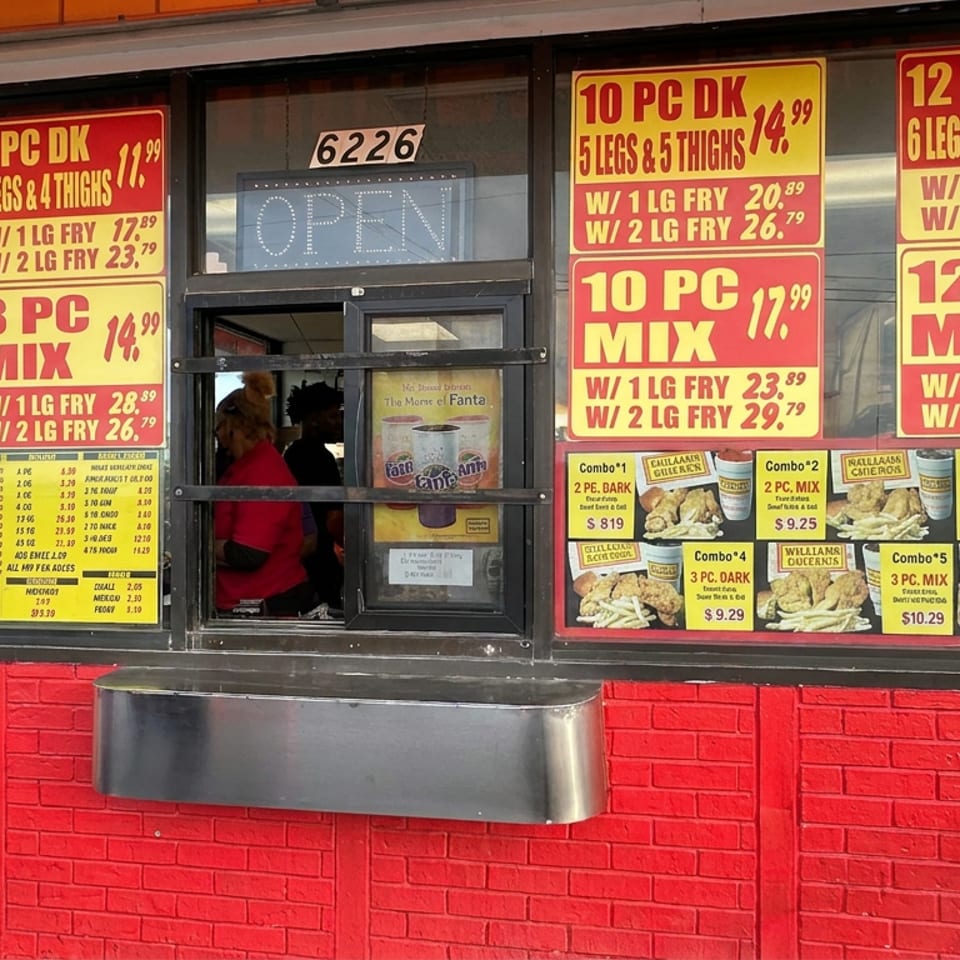 Restaurant drive-through window displays fried chicken meal menus, combo prices, and an illuminated open sign.
